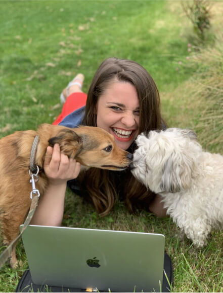Foto van copywriter Sylvie Van den broeck die in het gras ligt met haar laptop en haar twee hondjes.